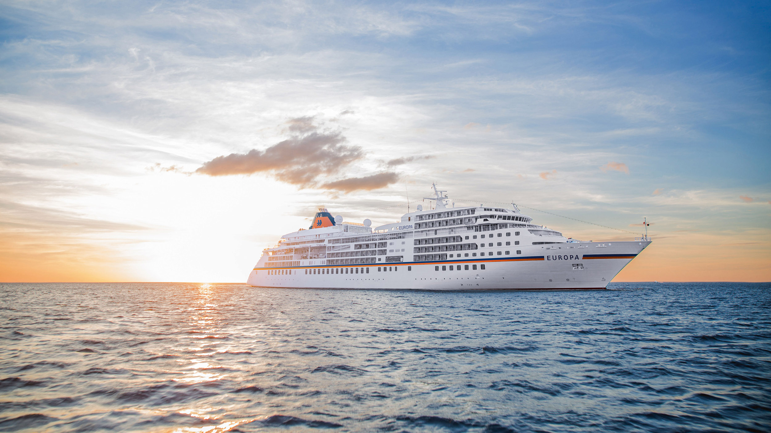 Zu sehen ist die MS Europa in Seitenansicht bei Sonnenuntergang auf hoher See.