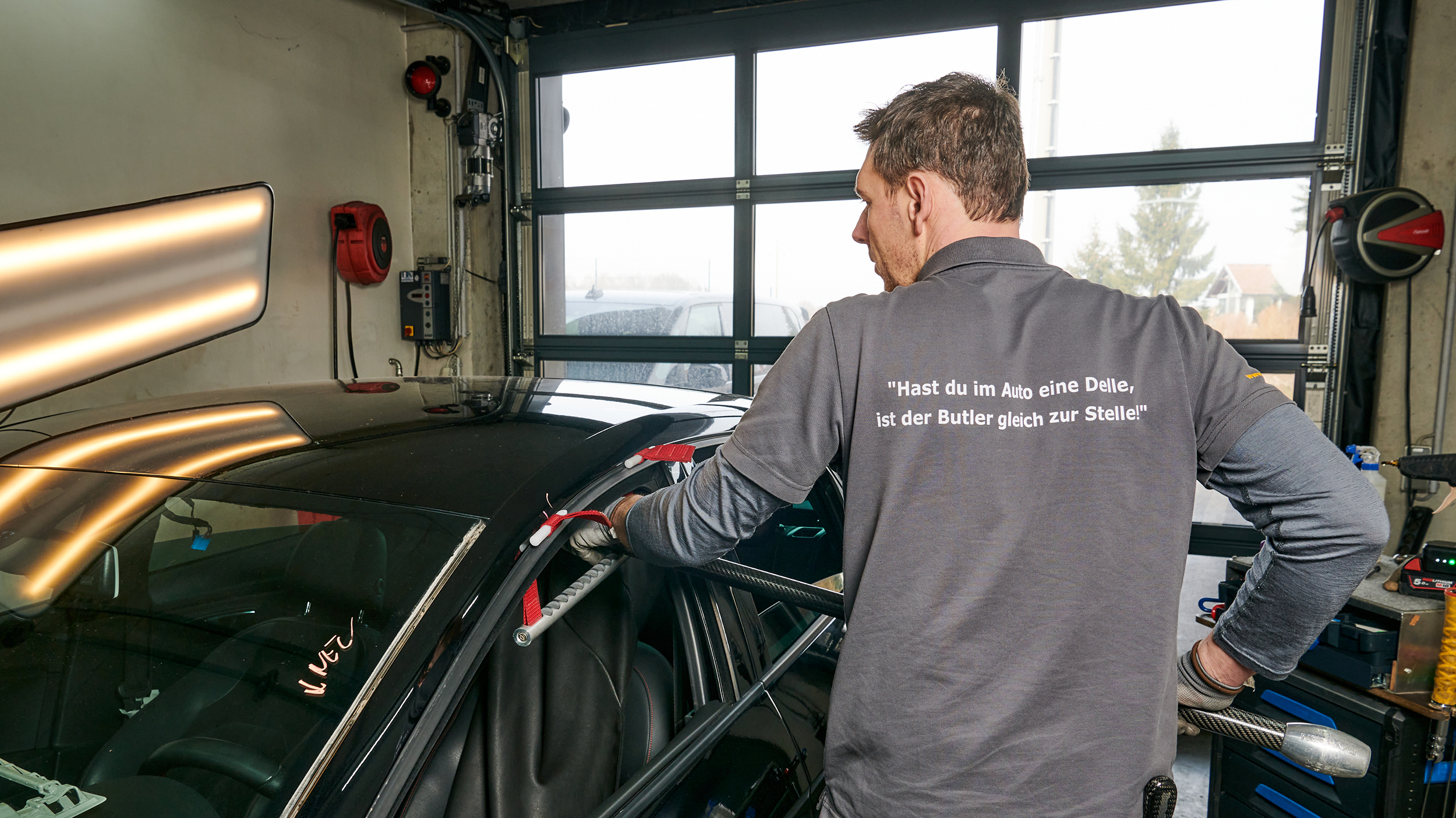 Ein Mann in der Werkstatt drückt eine Delle am Autodach mit Hilfe eines Werkzeugs aus.