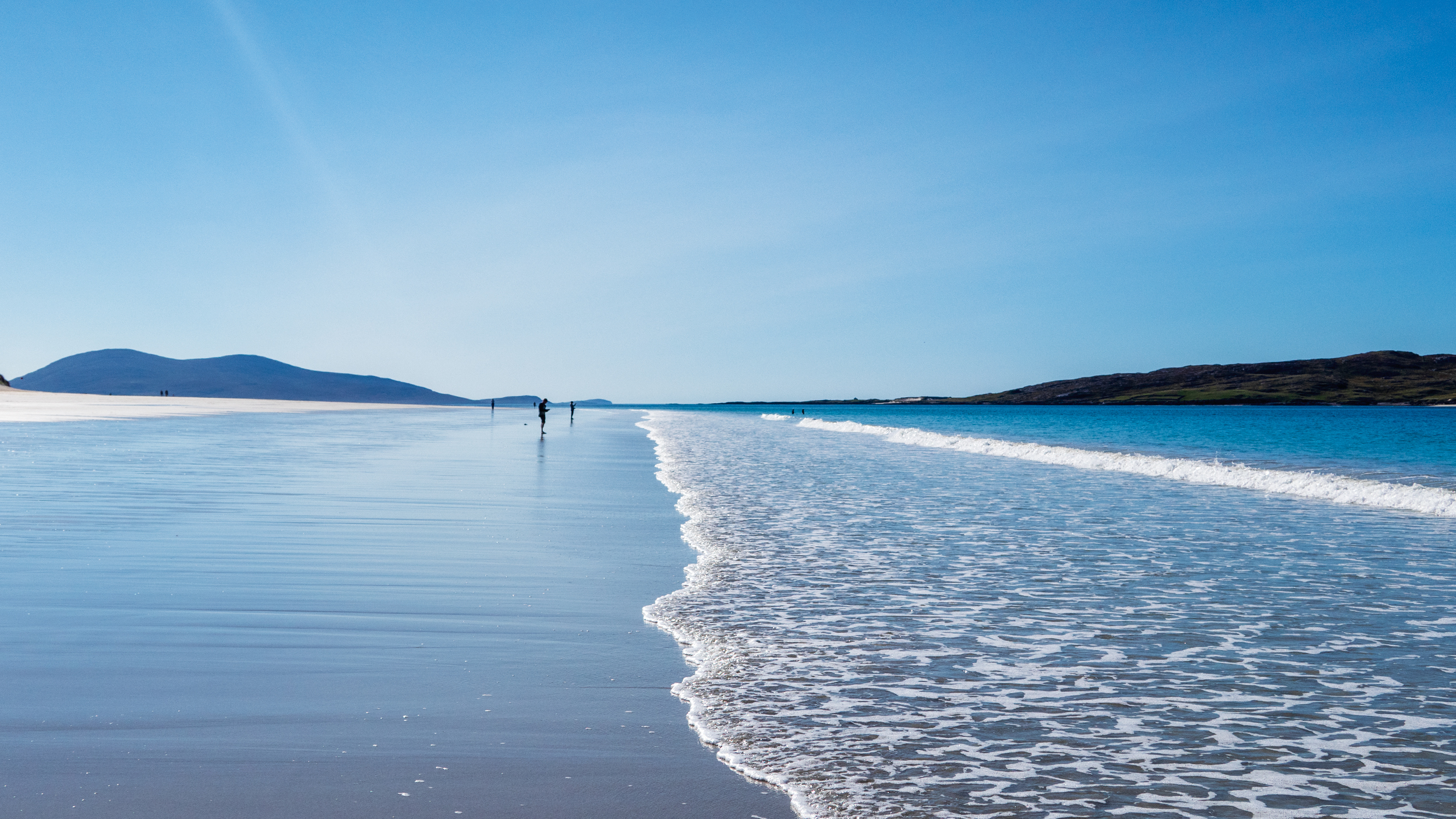 Ein breiter Sandstrand an einem schönen Tag mit blauem Himmel, der in einem blitzblauen Meer mündet.