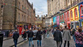 Die Victoria Street in Edinburgh, Schottland, mit vielen bunten Hauseingängen. Viele Menschen spazieren auf der Straße.