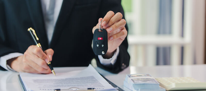 Jemand unterschreibt etwas und hält mit der anderen Hand einen Autoschlüssel