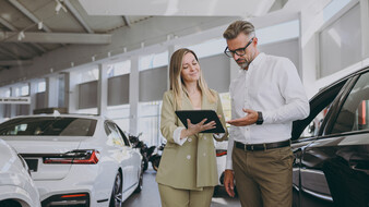 Eine Frau und ein Mann gehen in einem Autohaus Unterlagen durch