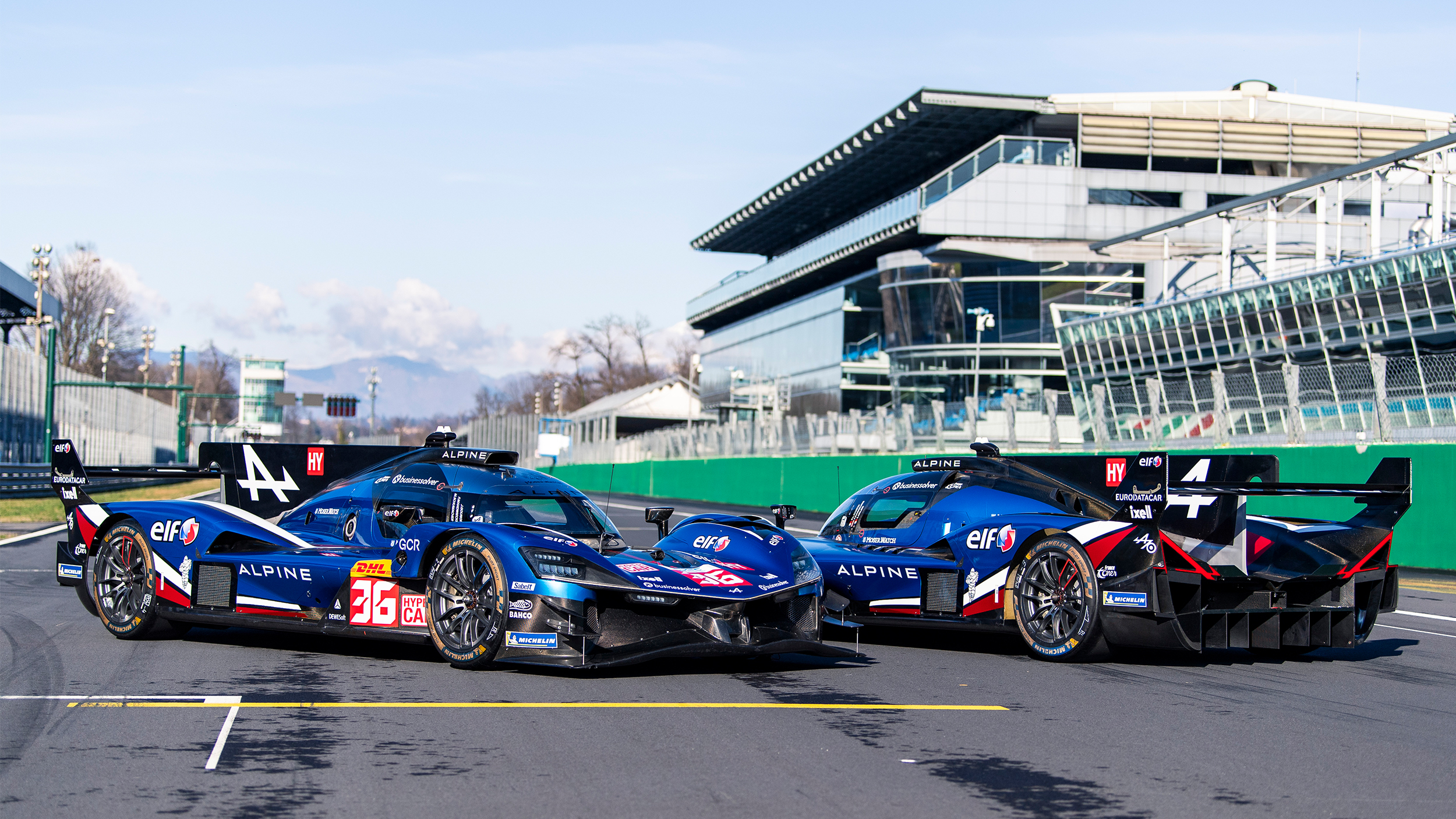 Zwei blaue Langstrecken-Rennwagen der Marke Alpine stehen auf der Start-Ziel-Gerade einer Rennstrecke.