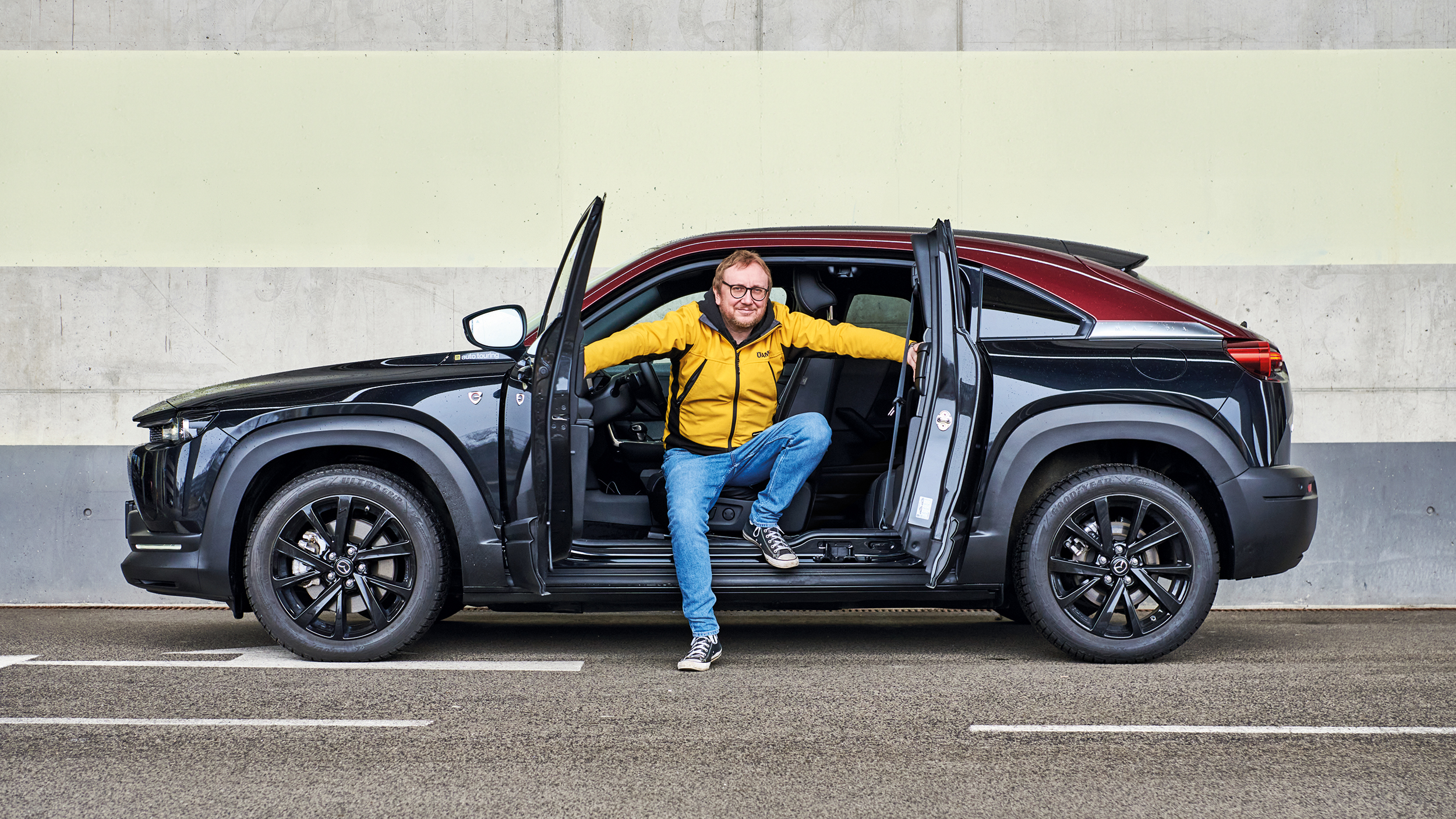 Eine Person sitzt in einem Mazda MX-30, dessen Türen gegenläufig geöffnet sind.