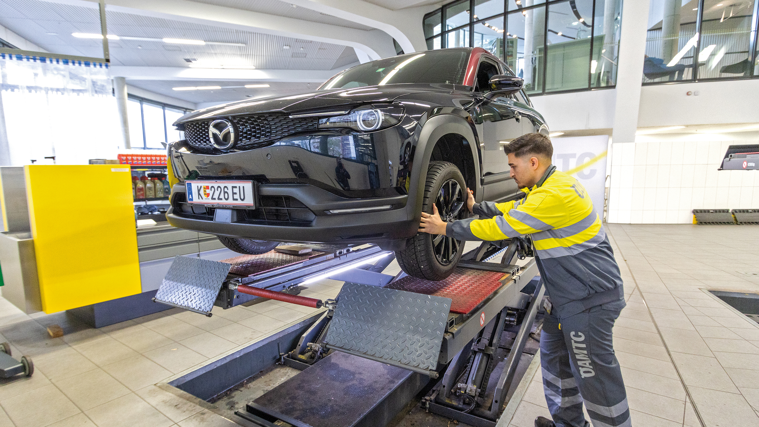 Ein ÖAMTC-Techniker montiert das Rad eines schwarz-roten SUV ab, das auf einer Hebebühne steht.