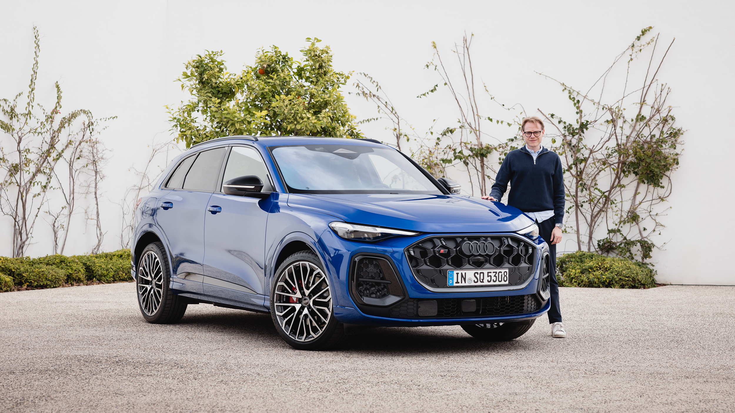 Eine Person steht neben einem blauen Audi Q5, der vor einer weißen Wand steht.