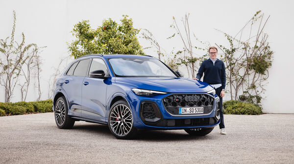 Eine Person steht neben einem blauen Audi Q5, der vor einer weißen Wand steht.