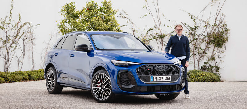 Eine Person steht neben einem blauen Audi Q5, der vor einer weißen Wand steht.