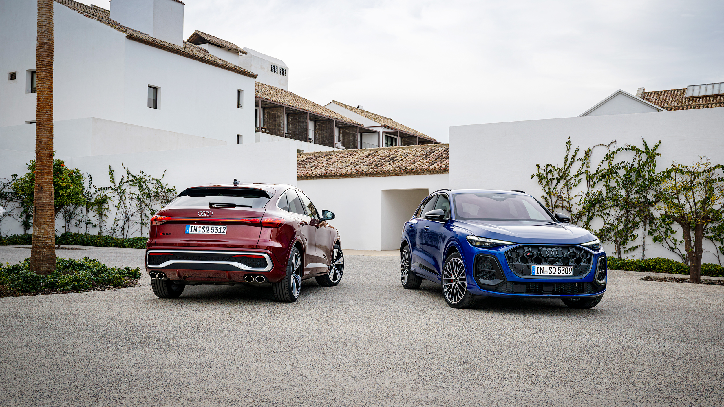 Ein roter und ein blauer Audi Q5 stehen vor einem weißen Gebäudekomplex.