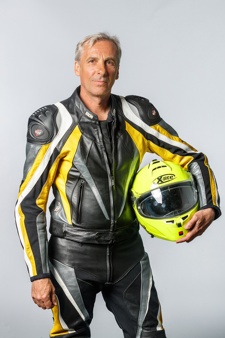 Porträt eines Mannes mit grauem Haar in voller Motorradmontur mit einem Helm in der Hand