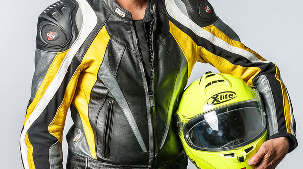 Porträt eines Mannes mit grauem Haar in voller Motorradmontur mit einem Helm in der Hand