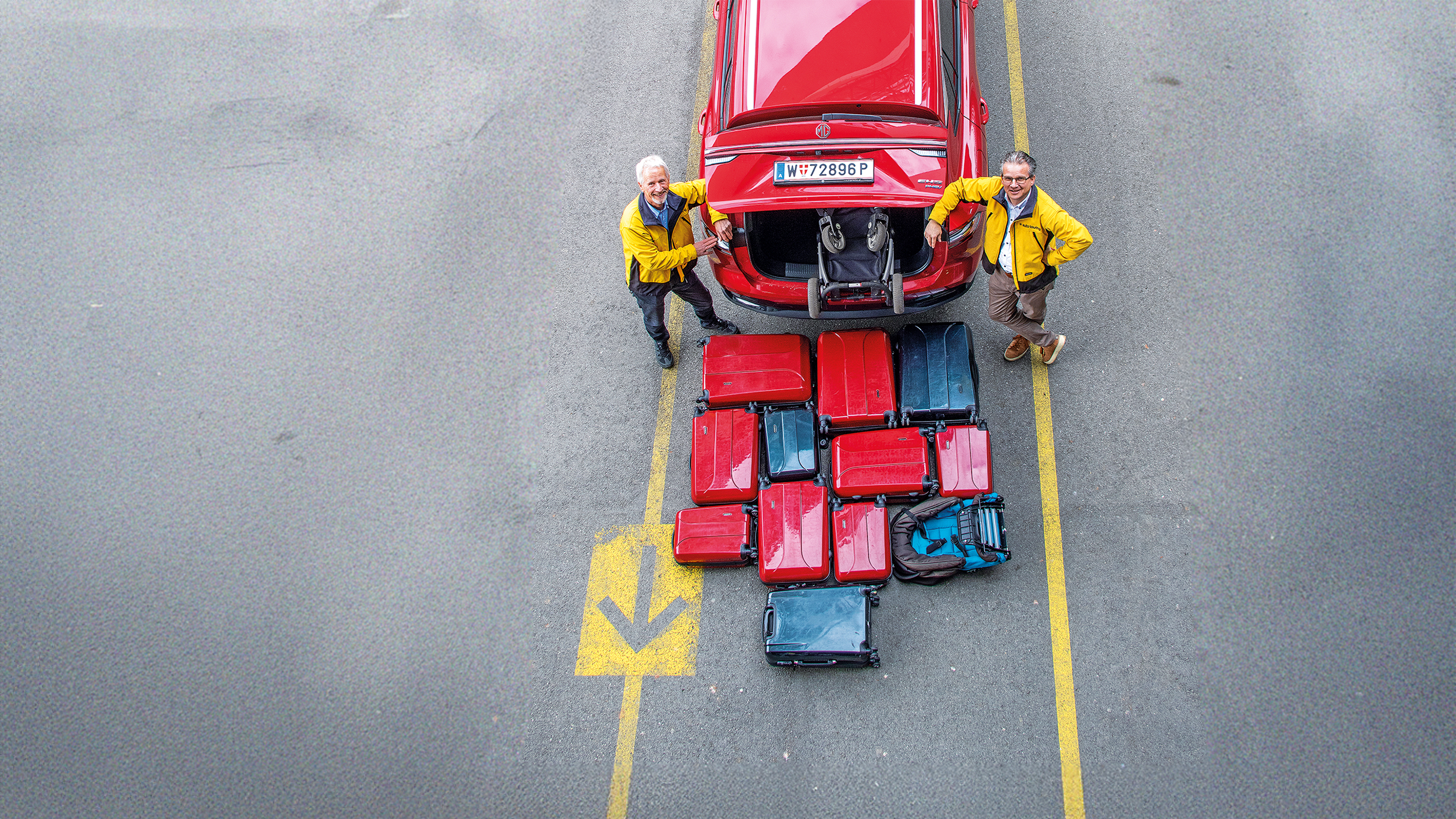 Heckansicht eines Autos von oben. Reisekoffer liegen vor dem Kofferraum.