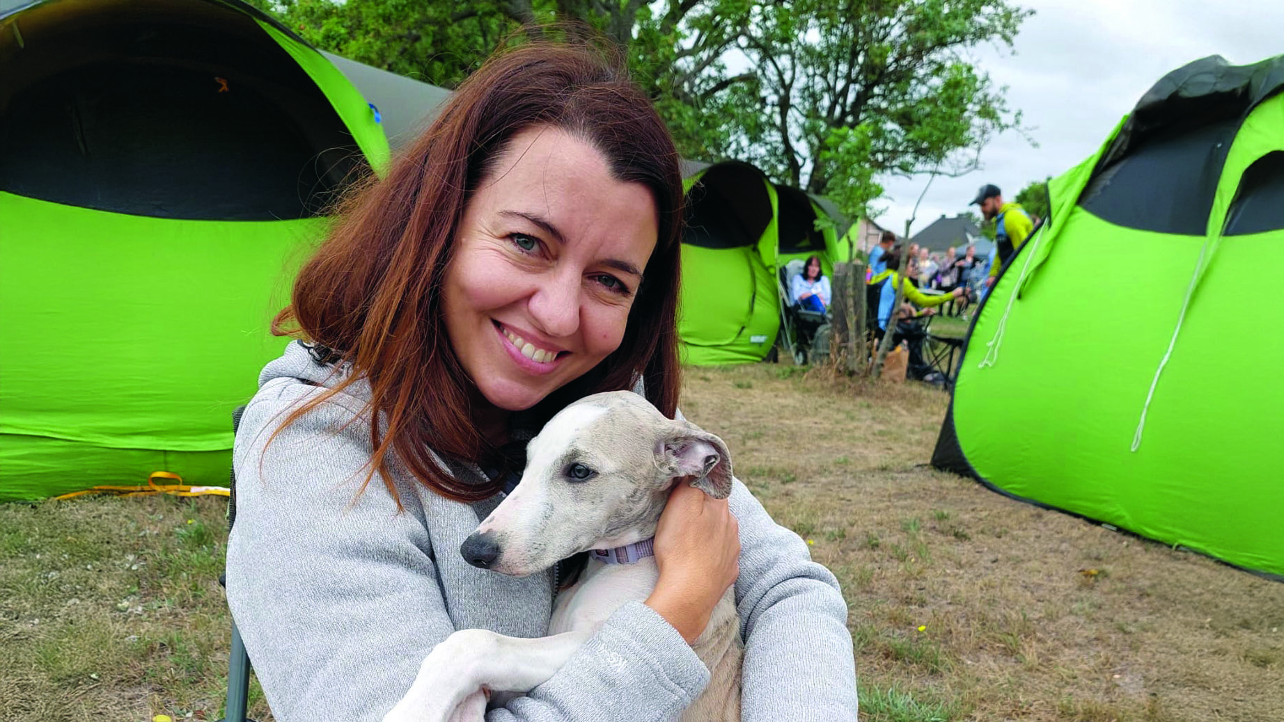 Eine braunhaarige Frau umarmt einen Hund auf einem Campingplatz
