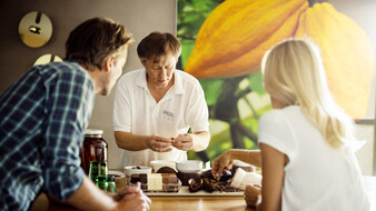 Ein Mann erklärt einem Pärchen wie Pralinen hergestellt werden.