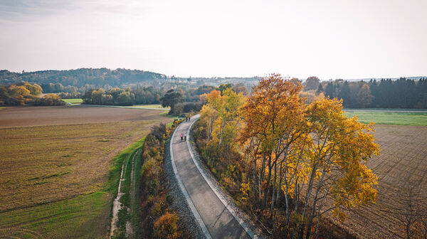 Bahntrassen-Radweg aus der Vogelperspektive. Es ist eine herbstliche Wettersituation, man sieht klein ein paar Fahrradfahrer:innen.