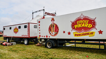 Zwei weiße LKW-Anhänger mit Bild des Zirkusdirektors und Logo vom Cirkus Pikard stehen auf einer Wiese.