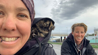 Selfie von Tanja Willers. Im Vordergrund ist sie zu sehen, auf ihrer Schulter sitzt eine Katze, daneben ihre Partnerin Johanna. Im Hintergrund eine Brücke.