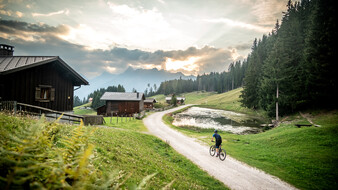 Ein Radfahrer fährt auf einem Radweg an Almhütten vorbei