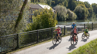Vier Radfahrer fahren auf einem Radweg an einem Fluss entlang