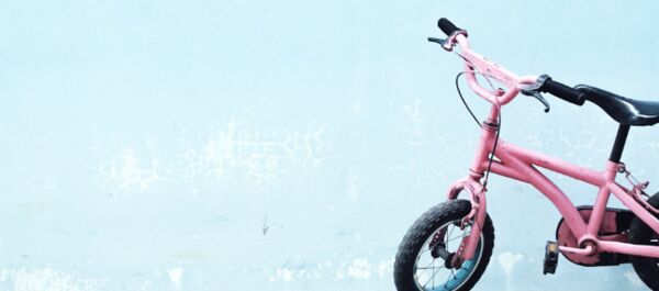Auf dem Bild ist ein rosa Kinderfahrrad vor einem hellblauen Hintergrund zu sehen.