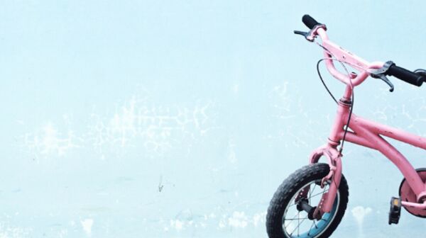 Auf dem Bild ist ein rosa Kinderfahrrad vor einem hellblauen Hintergrund zu sehen.
