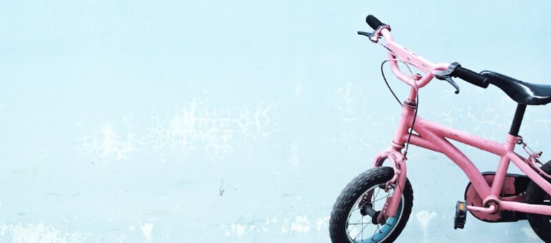 Auf dem Bild ist ein rosa Kinderfahrrad vor einem hellblauen Hintergrund zu sehen.