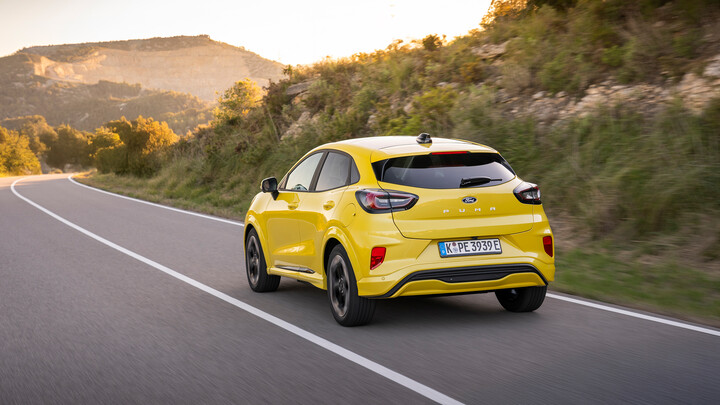 Ein gelber Ford Puma Gen-E fährt eine Landstraße entlang.