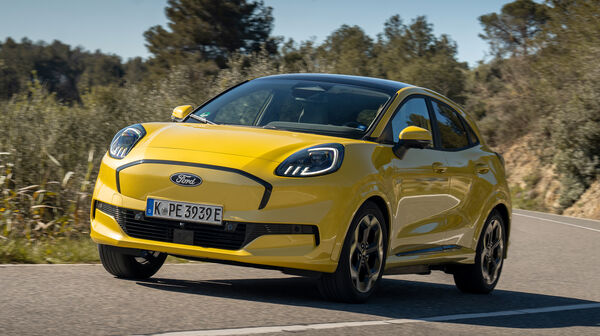 Ein gelber Ford Puma Gen-E fährt durch eine Kurve auf einer Landstraße.