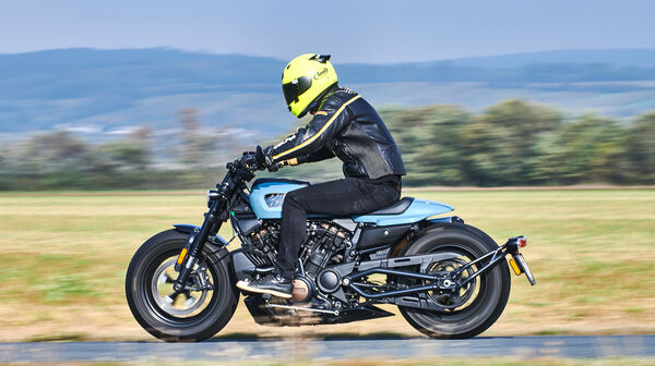 Seitlich fotografiertes, fahrendes, blau-schwarzes Motorrad.