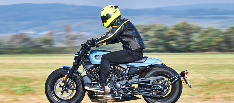 Seitlich fotografiertes, fahrendes, blau-schwarzes Motorrad.