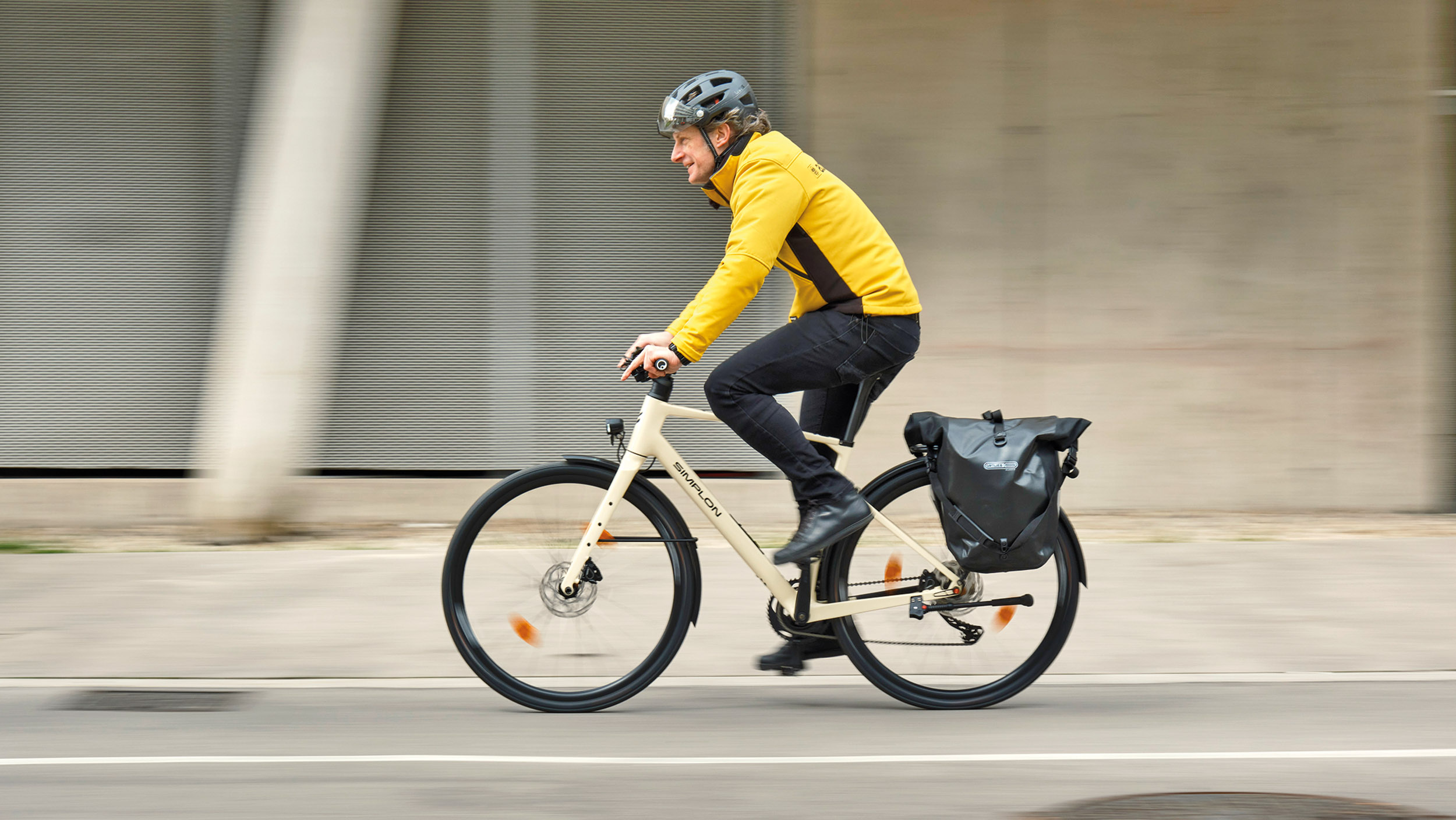 Seitlich fotografiertes, fahrendes Fahrrad mit schwarzen Gepäcktaschen.