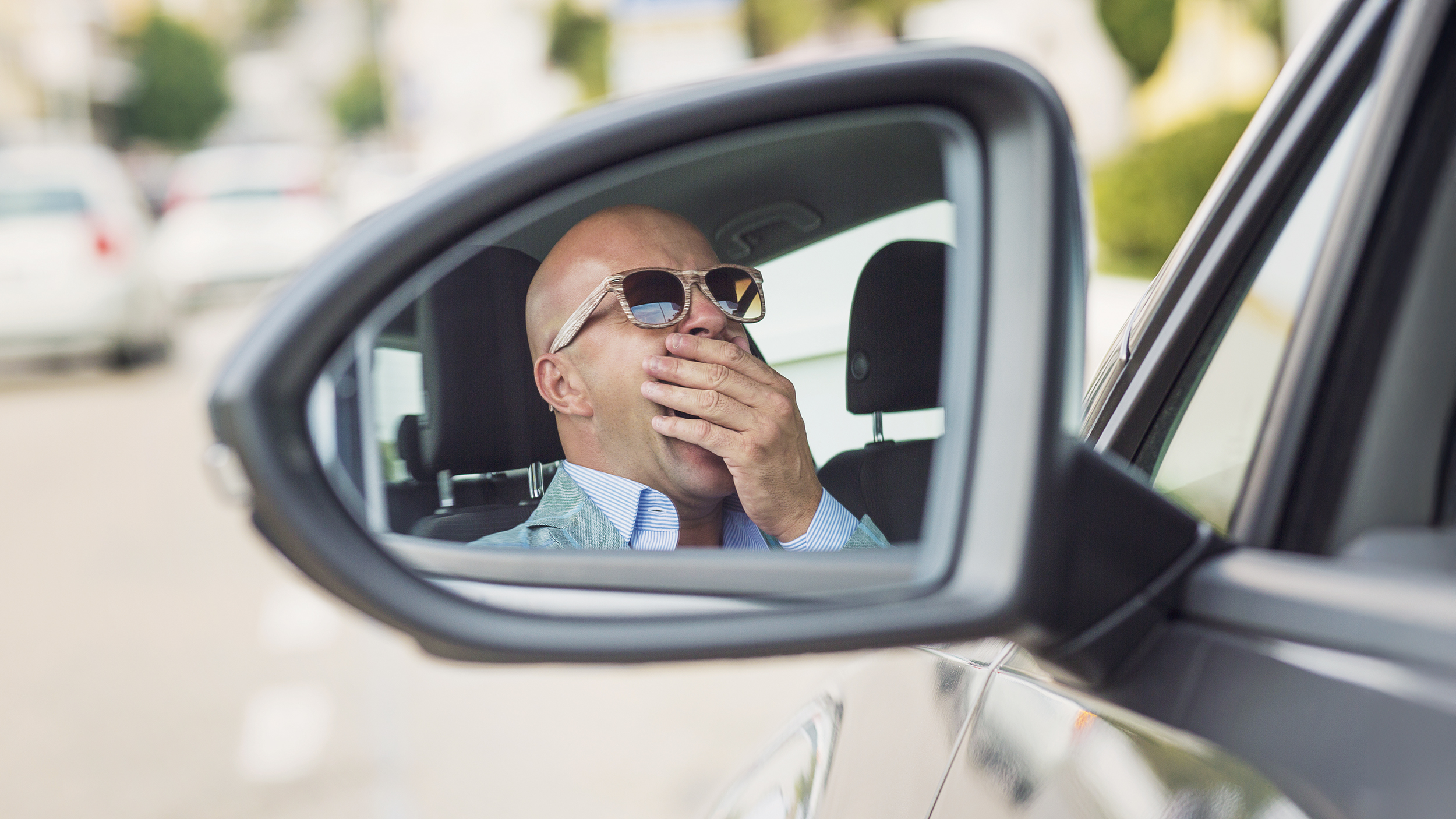 Mann mit Sonnenbrille sitzt gähnend im Auto.