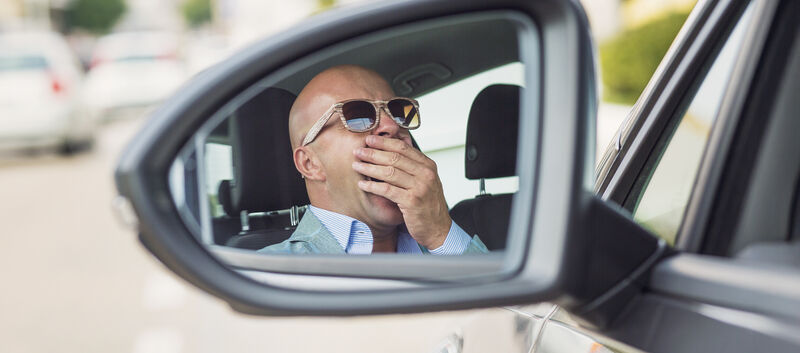 Mann mit Sonnenbrille sitzt gähnend im Auto.