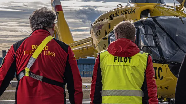 Auf dem Bild sieht man drei Crewmitglieder der ÖAMTC-Flugrettung von hinten, wie sie auf einen Hubschrauber zugehen.