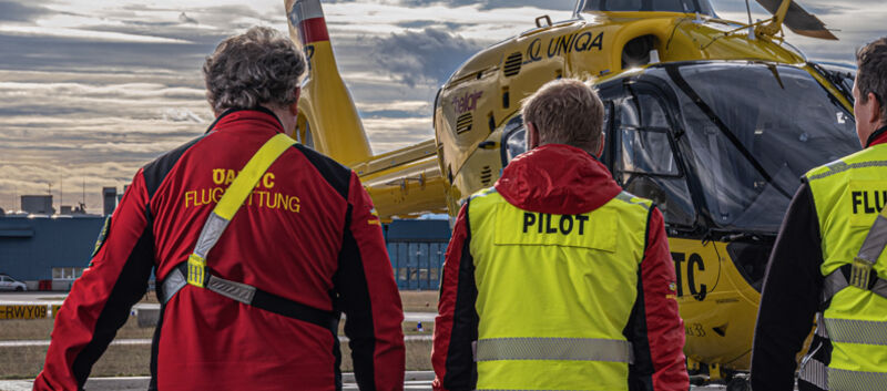 Auf dem Bild sieht man drei Crewmitglieder der ÖAMTC-Flugrettung von hinten, wie sie auf einen Hubschrauber zugehen.