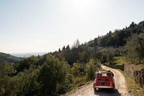 Auf dem Bild sieht man einen roten Fiat 500 von hinten, der auf einer Sandstraße in der Natur steht.