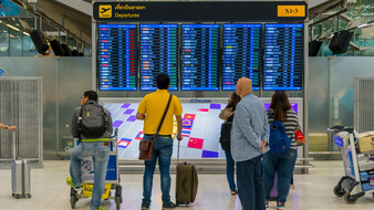 Einige Fluggäste stehen vor der Tafel am Flughafen und schauen wann ihr Flug abfliegt.