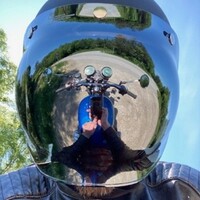 Auf dem Bild sieht man den Kopf einer Person die einen verspiegelten Motorradhelm trägt. Im Visier spiegelt sich ein blaues Motorrad.