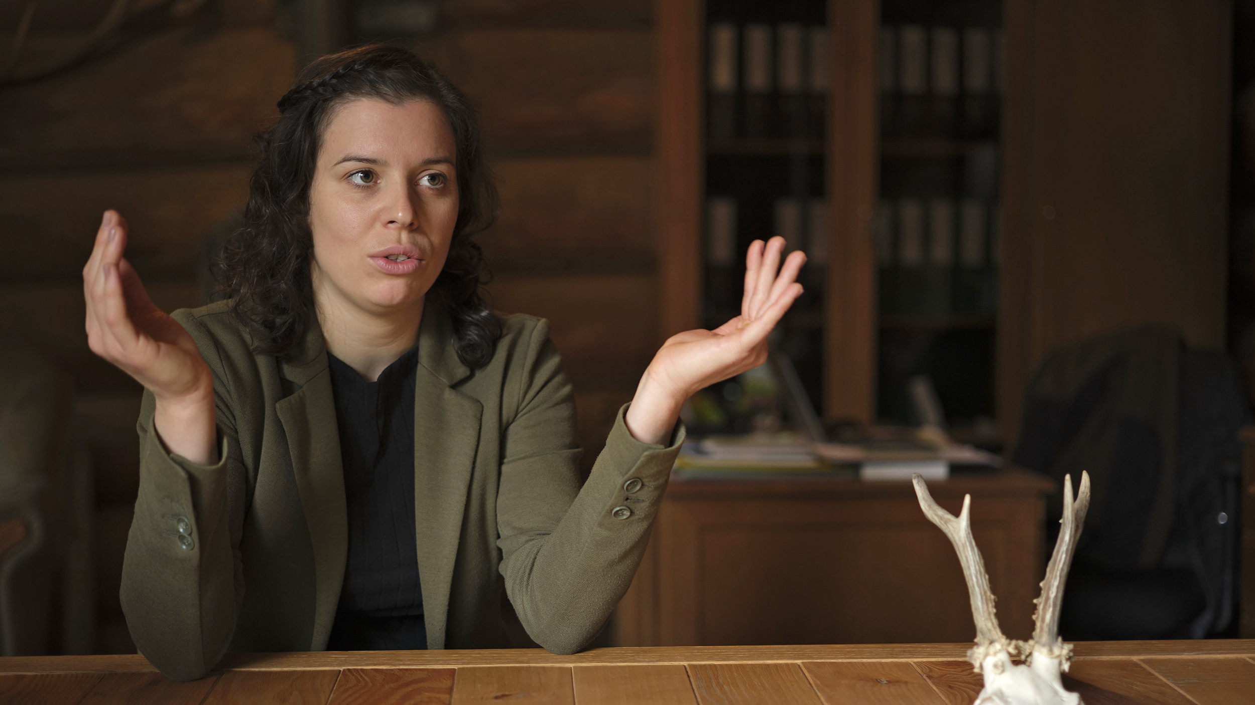 Försterin Stefanie Nievoll gestikuliert mit den Händen beim Interview in ihrem Büro in der Blockhütte. Am Tisch liegt ein Rehbockgeweih.