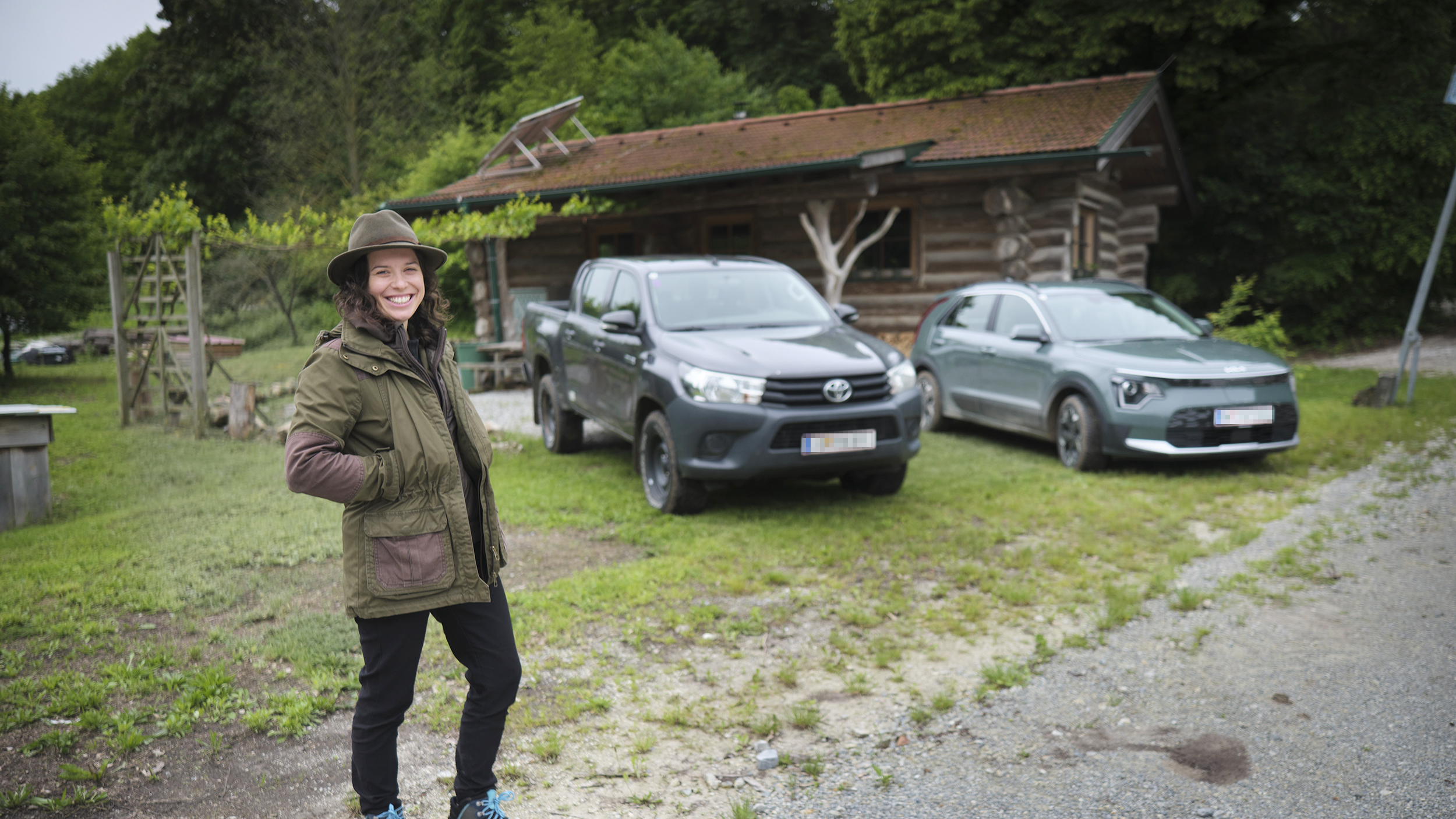 Försterin Stefanie Nievoll steht vor ihren Dienstfahrzeugen Kia Niro. Im Hintergrund der zweite Dienstwagen, ein Toyota Hilux und eine Blockhütte.