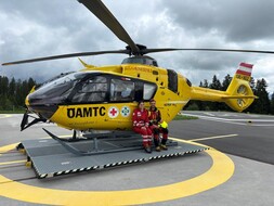 Eine junge Frau in Rotkreuz-Uniform und ein junger Mann in der Uniform der ÖAMTC-Flugrettung sitzen auf der Kufe eines ÖAMTC Notarzthubschraubers