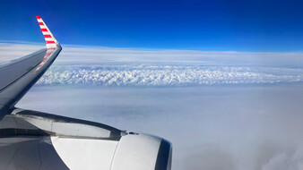 Blick auf den Himmel vom Flugzeug aus. Man sieht leicht die Tragfläche.