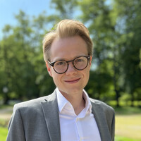 Eine Person im grauen Anzug steht vor einem Baum.