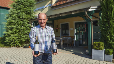 Winzer Manfred Edelmann präsentiert im Hof seines Betriebs zwei Weinflaschen, eine mit Chardonnay und eine mit einer Rotwein-Cuvée.