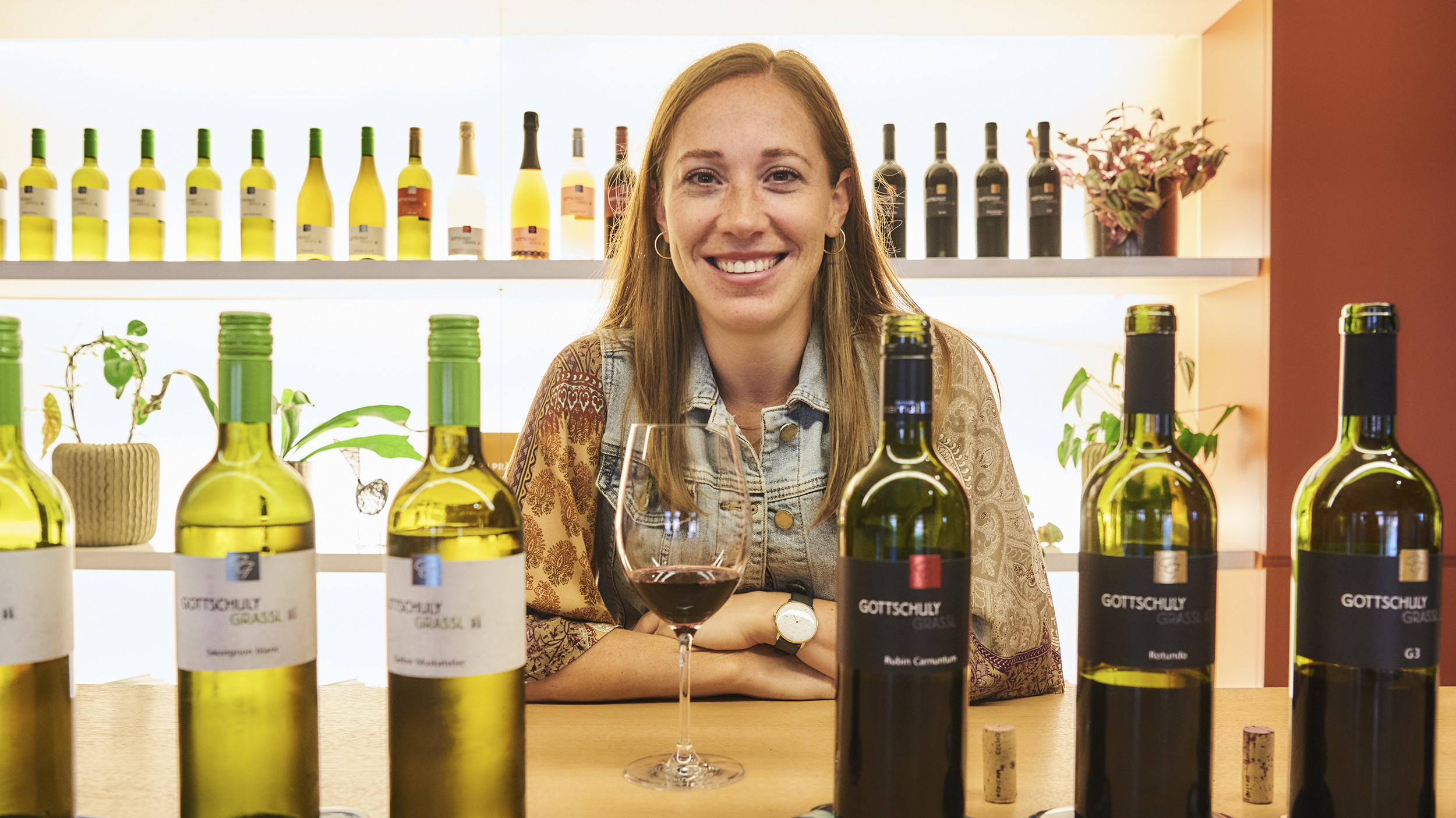 Hinter den Weinflaschen lächelt die Winzerin Victoria Gottschuly-Grassl in die Kamera.
