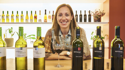 Hinter den Weinflaschen lächelt die Winzerin Victoria Gottschuly-Grassl in die Kamera.