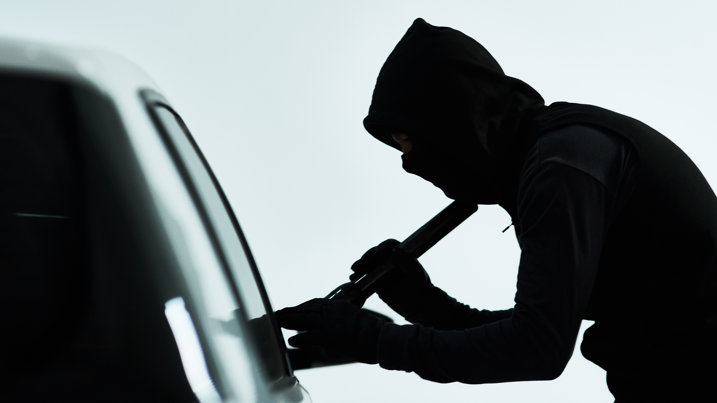 Silhouette eines vemummten Mannes, der ein Auto knackt
