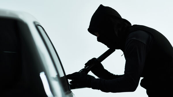 Silhouette eines vemummten Mannes, der ein Auto knackt