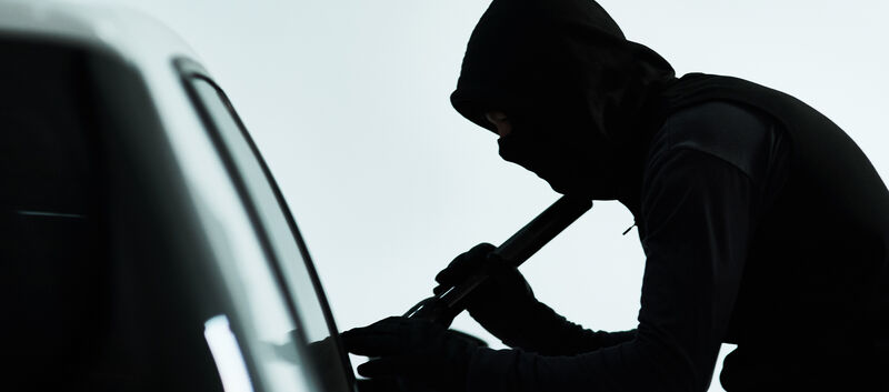 Silhouette eines vemummten Mannes, der ein Auto knackt