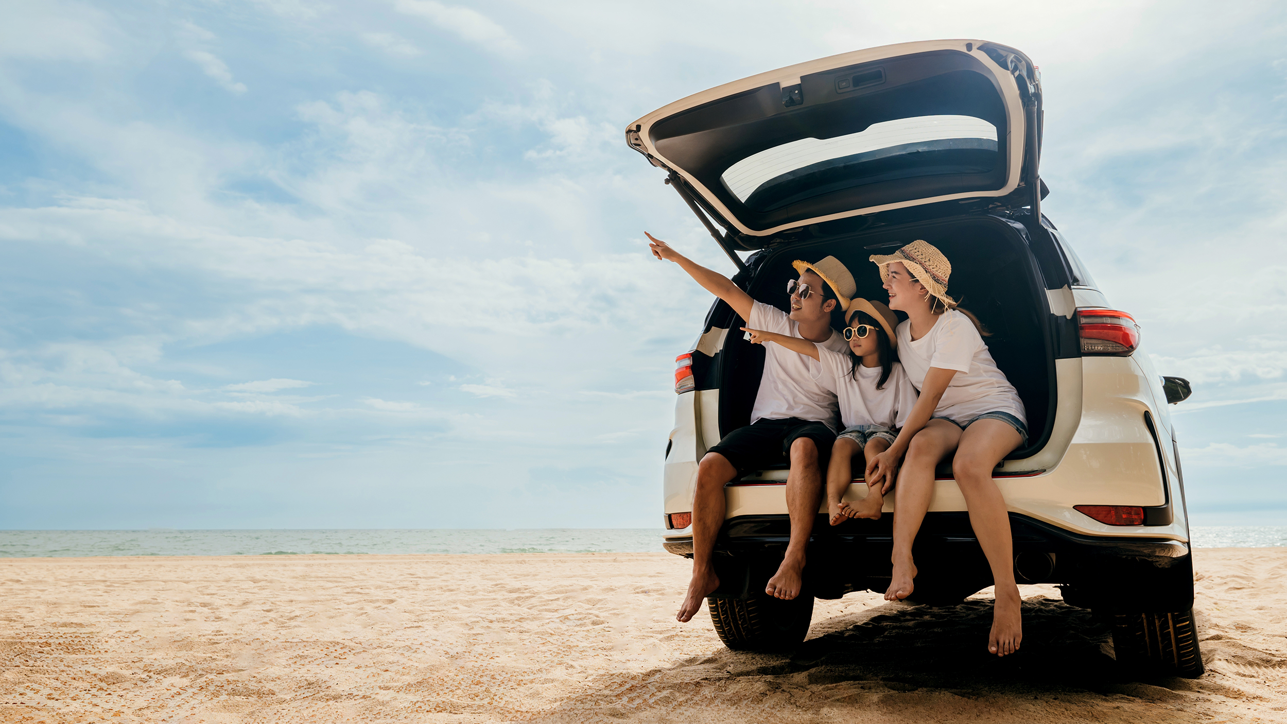 Eine Mutter mit zwei Kindern sitzt im Kofferraum eines Autos am Strand